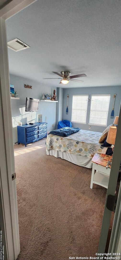 carpeted bedroom featuring ceiling fan and a textured ceiling