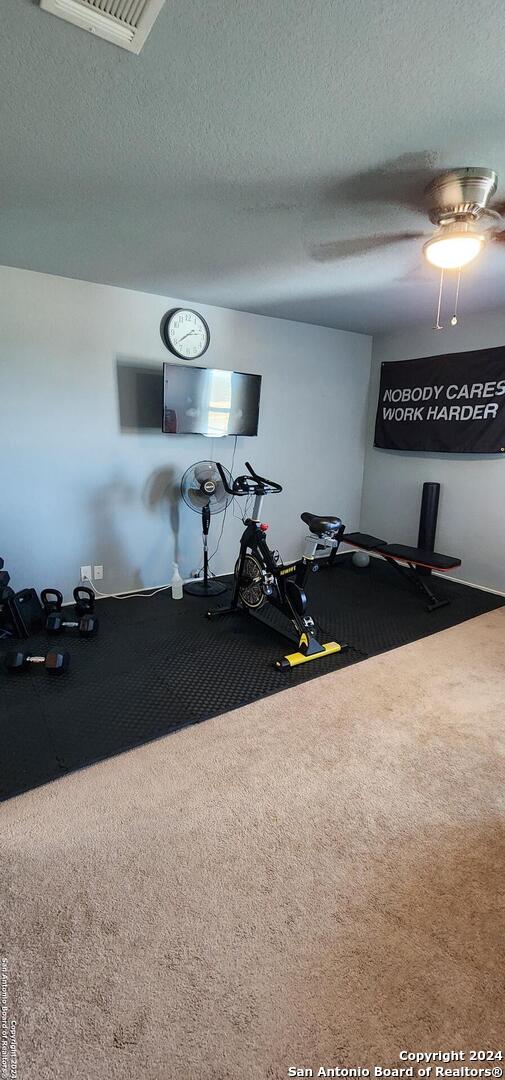 exercise room featuring ceiling fan, a textured ceiling, and carpet