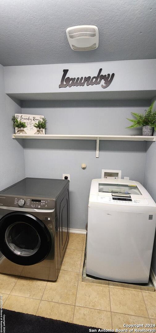 washroom with a textured ceiling, light tile patterned floors, and washer and dryer