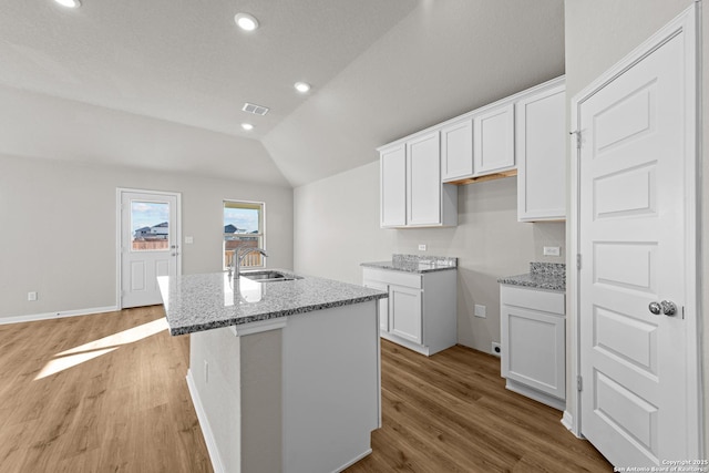 kitchen featuring an island with sink, lofted ceiling, sink, white cabinets, and light stone countertops