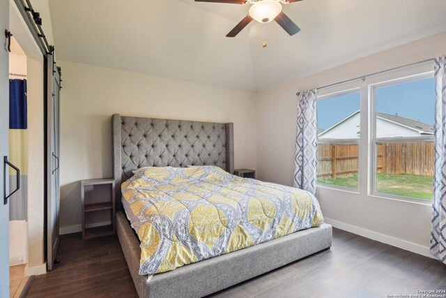 bedroom featuring dark hardwood / wood-style floors, vaulted ceiling, a barn door, and ceiling fan