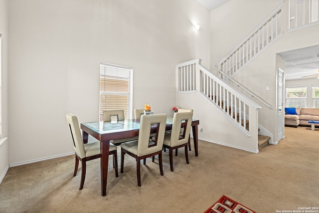 carpeted dining room with ceiling fan and a towering ceiling