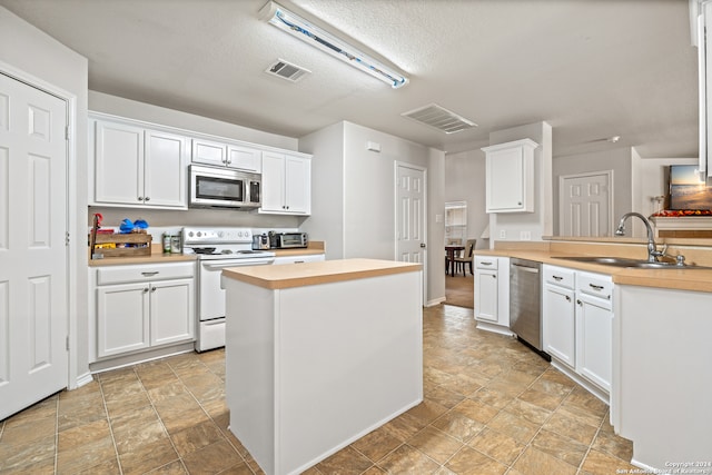 kitchen featuring stainless steel appliances, sink, kitchen peninsula, light tile patterned flooring, and white cabinetry