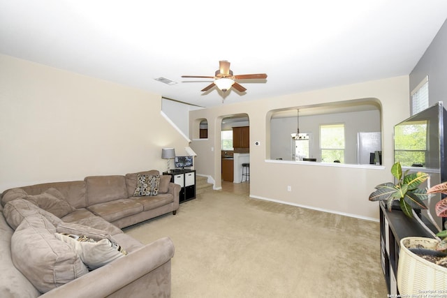 carpeted living room with ceiling fan with notable chandelier