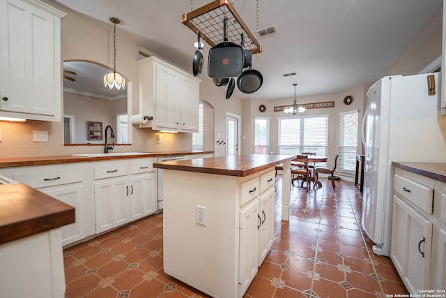 kitchen with decorative light fixtures, tile patterned floors, white refrigerator, white cabinets, and a kitchen island