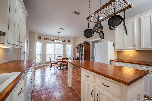 kitchen featuring white appliances, wooden counters, a kitchen island, white cabinetry, and a notable chandelier