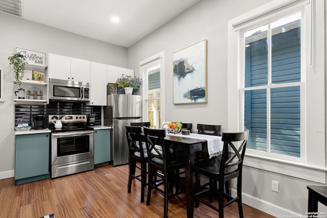 kitchen featuring white cabinets, stainless steel appliances, wood-type flooring, and decorative backsplash