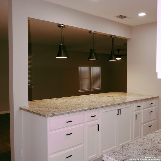 kitchen with decorative light fixtures, kitchen peninsula, light stone counters, and white cabinetry