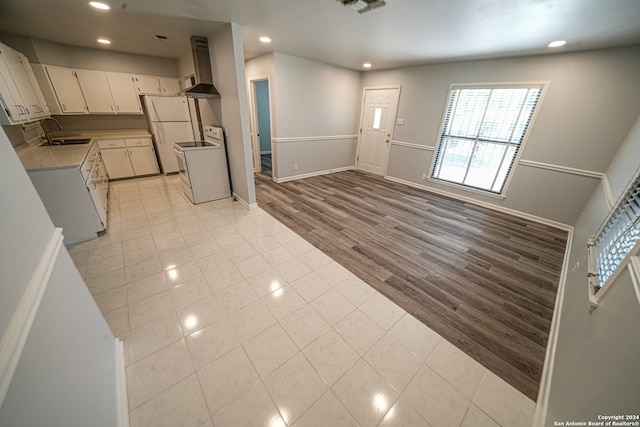 kitchen featuring white cabinetry, light hardwood / wood-style flooring, wall chimney range hood, white refrigerator, and sink