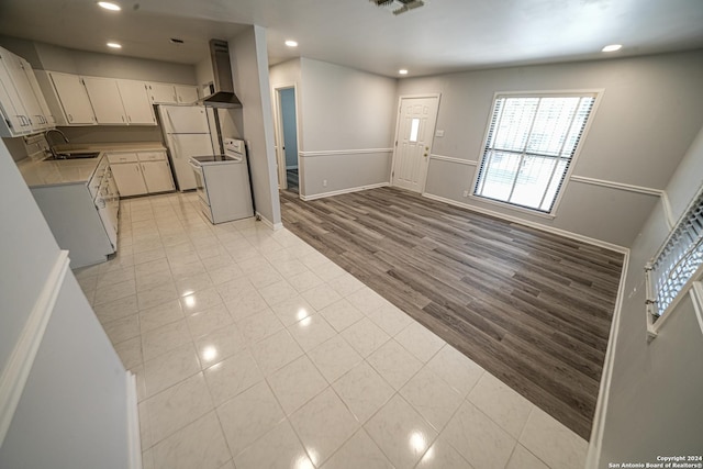 kitchen with light tile patterned flooring, sink, white cabinets, white appliances, and wall chimney range hood