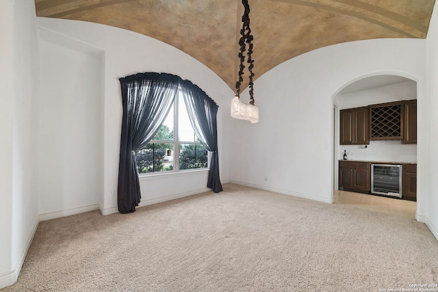 carpeted spare room featuring wine cooler, vaulted ceiling, and indoor bar