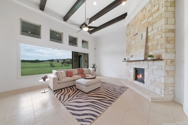 tiled living room featuring ceiling fan, a high ceiling, beamed ceiling, and a stone fireplace