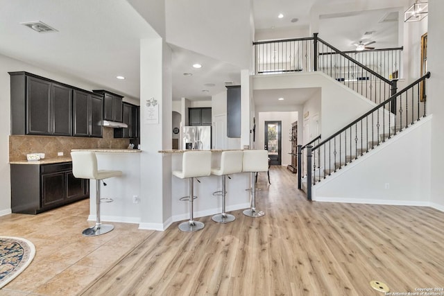 kitchen featuring stainless steel fridge, backsplash, a kitchen breakfast bar, light hardwood / wood-style floors, and kitchen peninsula