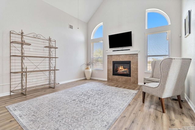 sitting room featuring a tiled fireplace, hardwood / wood-style flooring, high vaulted ceiling, and a healthy amount of sunlight