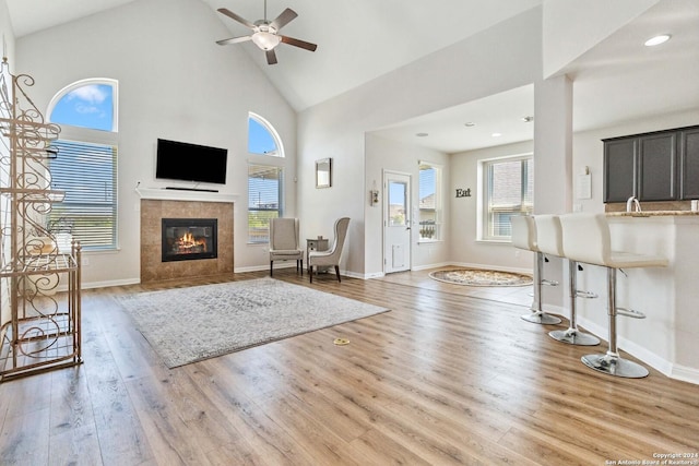 unfurnished living room with sink, high vaulted ceiling, light wood-type flooring, ceiling fan, and a fireplace