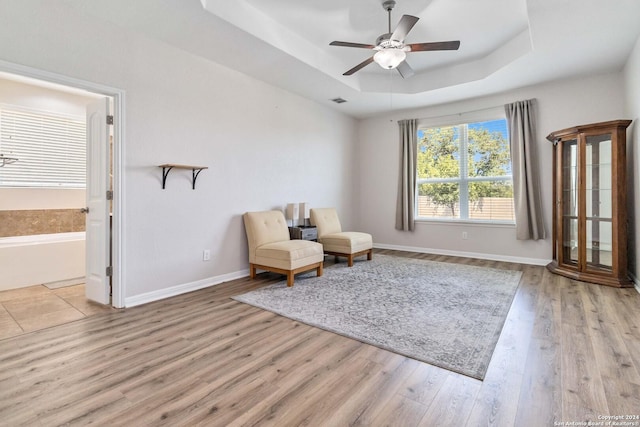 living area with light hardwood / wood-style floors, a raised ceiling, and ceiling fan