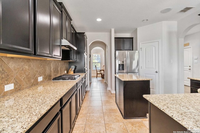 kitchen featuring tasteful backsplash, light tile patterned floors, stainless steel appliances, light stone countertops, and dark brown cabinets