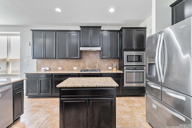 kitchen with light tile patterned floors, appliances with stainless steel finishes, light stone countertops, a kitchen island, and decorative backsplash