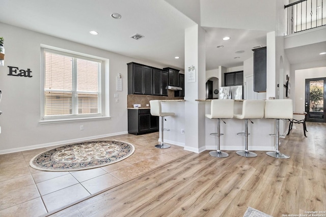 kitchen with tasteful backsplash, light hardwood / wood-style flooring, stainless steel refrigerator, a kitchen breakfast bar, and kitchen peninsula