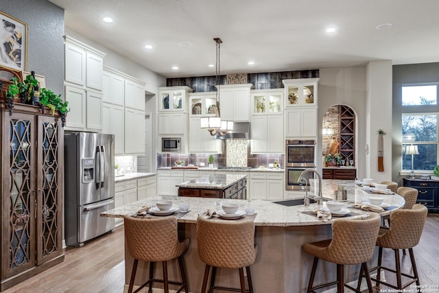 kitchen with appliances with stainless steel finishes, hanging light fixtures, a kitchen breakfast bar, light stone counters, and a center island with sink