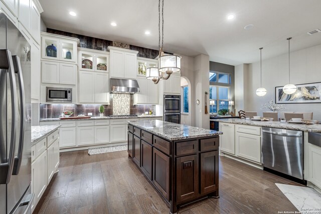 kitchen featuring dark brown cabinets, wall chimney range hood, stainless steel appliances, and dark wood-type flooring