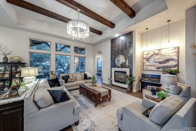 living room with an inviting chandelier, wood-type flooring, a raised ceiling, and a large fireplace