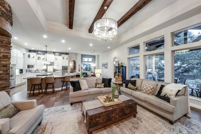 living room with a notable chandelier, light hardwood / wood-style flooring, beam ceiling, and a towering ceiling