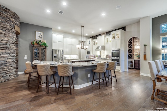 kitchen with hanging light fixtures, stainless steel appliances, wine cooler, a kitchen bar, and a large island with sink