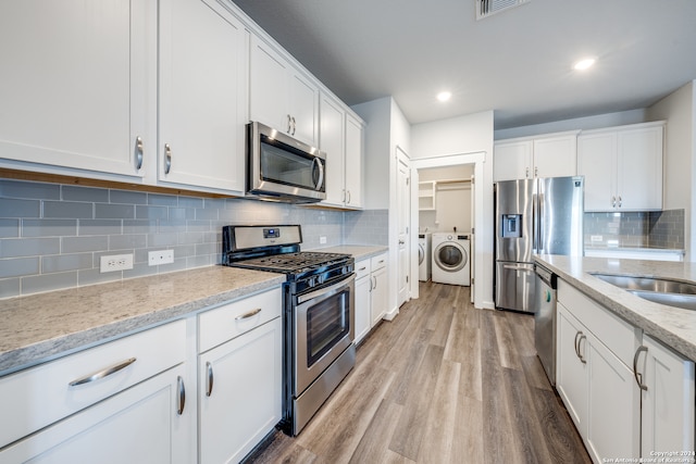 kitchen with light hardwood / wood-style flooring, white cabinets, washing machine and clothes dryer, backsplash, and stainless steel appliances