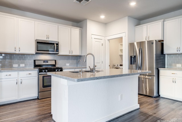 kitchen with appliances with stainless steel finishes, dark hardwood / wood-style floors, white cabinetry, washing machine and dryer, and a center island with sink