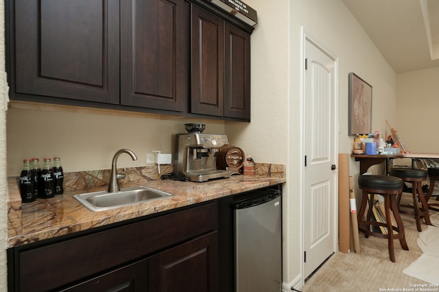 kitchen featuring dark brown cabinetry, light carpet, light stone counters, dishwasher, and sink