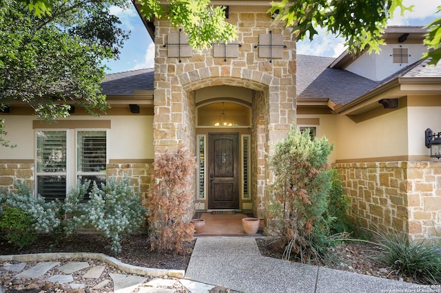 view of exterior entry featuring stone siding, a shingled roof, and stucco siding