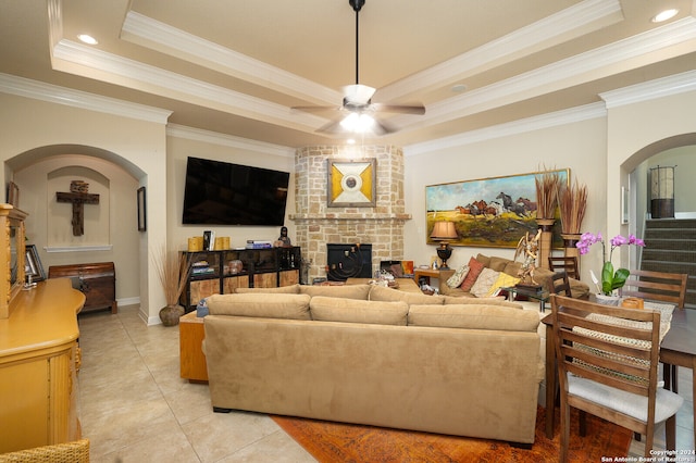 tiled living room featuring ceiling fan, brick wall, a brick fireplace, a tray ceiling, and ornamental molding