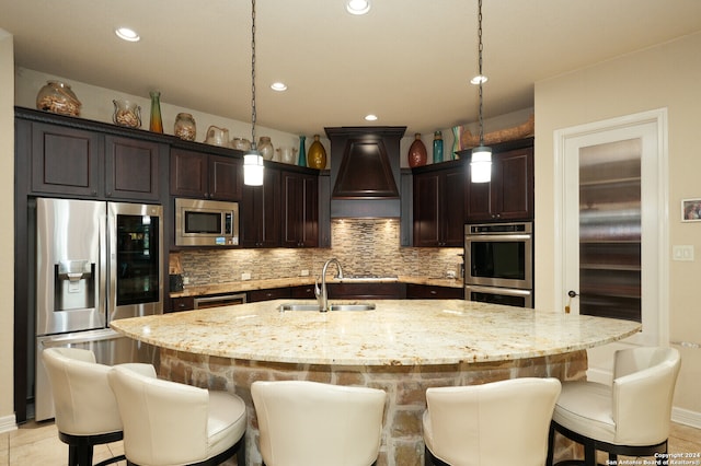 kitchen with custom range hood, appliances with stainless steel finishes, decorative backsplash, sink, and an island with sink