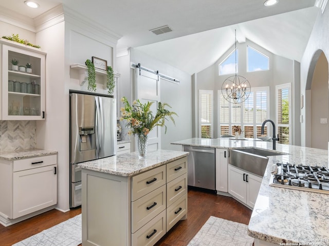 kitchen with light stone counters, a kitchen island with sink, dark wood-type flooring, stainless steel appliances, and a barn door