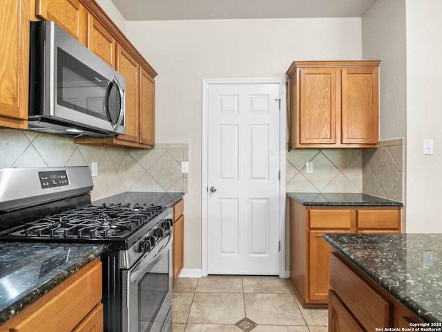 kitchen with light tile patterned flooring, stainless steel appliances, tasteful backsplash, and dark stone counters