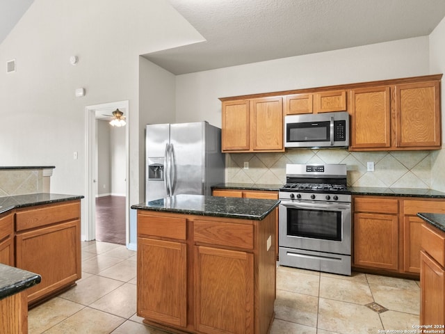 kitchen featuring light tile patterned flooring, dark stone counters, a kitchen island, stainless steel appliances, and decorative backsplash