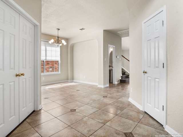 interior space with a notable chandelier, a textured ceiling, and light tile patterned flooring