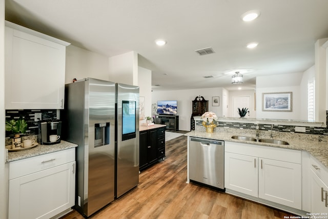 kitchen with sink, light stone counters, light hardwood / wood-style floors, white cabinets, and appliances with stainless steel finishes