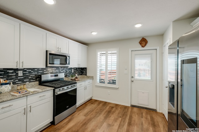 kitchen with appliances with stainless steel finishes, backsplash, light hardwood / wood-style flooring, and white cabinetry