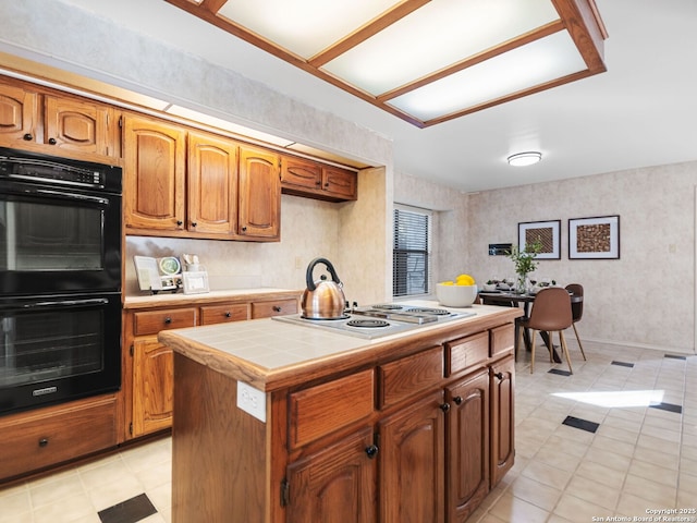 kitchen with stainless steel gas cooktop, tile countertops, a center island, light tile patterned floors, and double oven