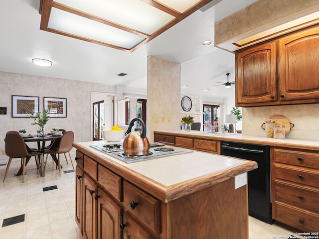 kitchen with stainless steel gas cooktop, tile counters, kitchen peninsula, dishwasher, and a kitchen island