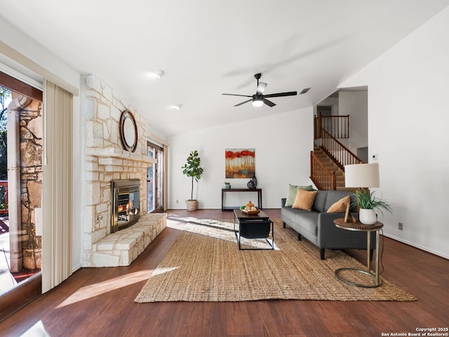 living room featuring hardwood / wood-style flooring, lofted ceiling, a stone fireplace, and ceiling fan