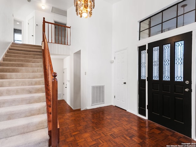 entryway featuring an inviting chandelier, a towering ceiling, and dark parquet floors