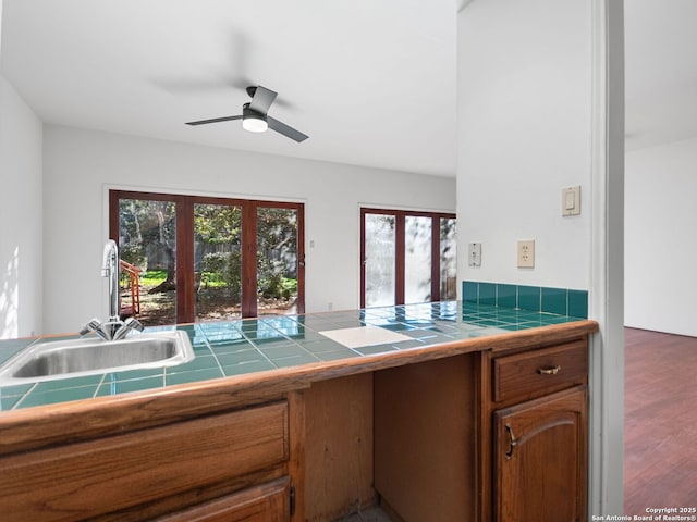 kitchen featuring sink, wood-type flooring, tile counters, and ceiling fan