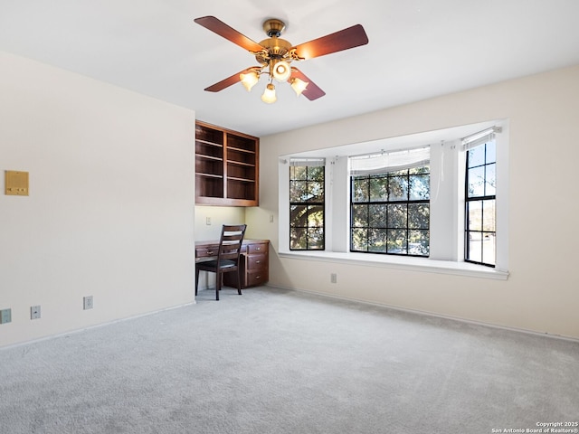 empty room with ceiling fan, built in desk, and carpet