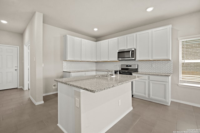 kitchen with light tile patterned flooring, stainless steel appliances, an island with sink, white cabinets, and decorative backsplash