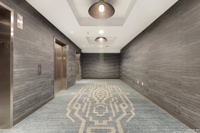 hallway with elevator and a tray ceiling