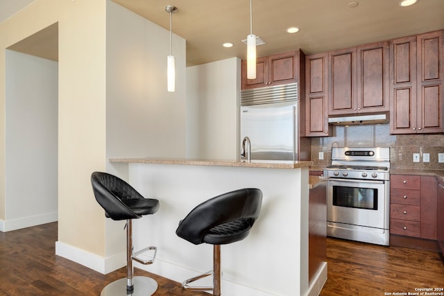 kitchen with appliances with stainless steel finishes, a kitchen bar, backsplash, hanging light fixtures, and dark hardwood / wood-style floors