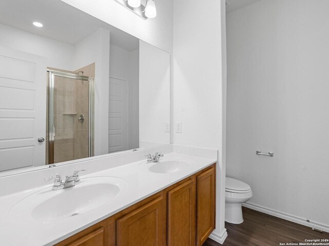 bathroom with an enclosed shower, dual bowl vanity, wood-type flooring, and toilet